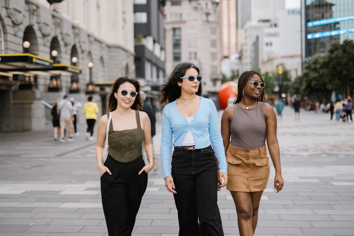 Three fashionable women walking through an urban street wearing Dresden Vision United States photochromic eyewear, designed for clarity, comfort, and automatic light adaptation.